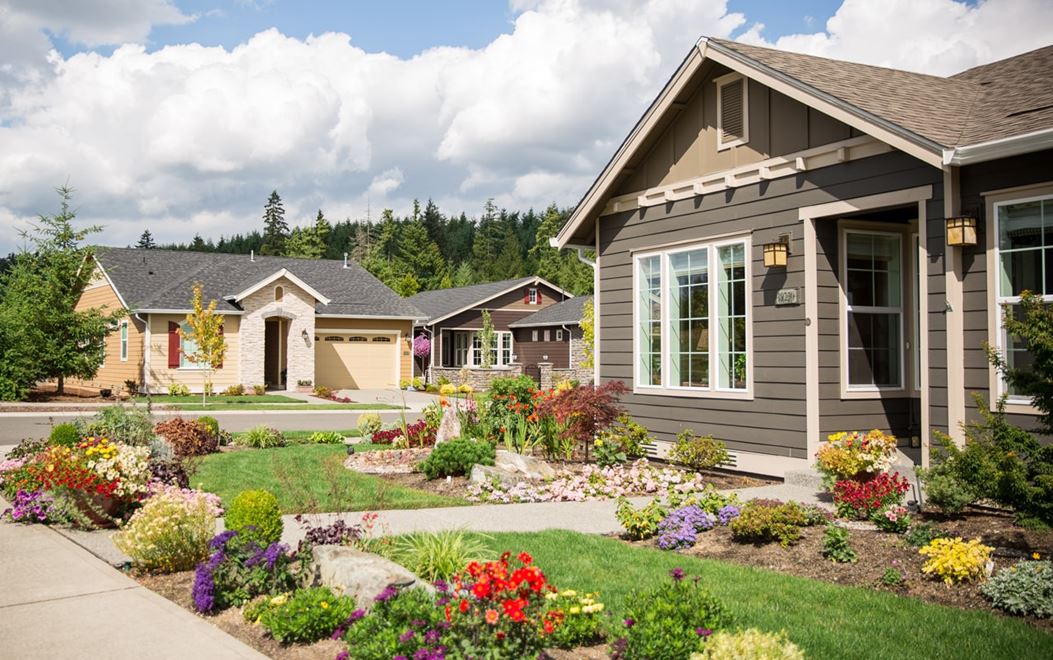 Gray one-story home with flower beds lining the yard and another home in the background