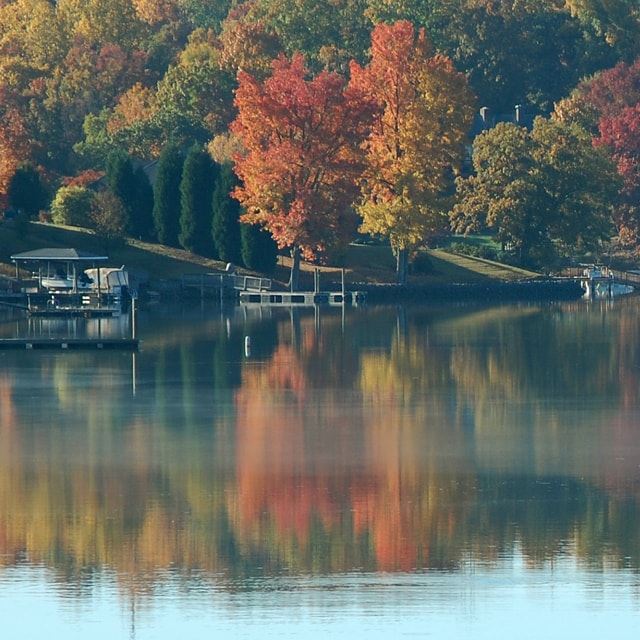 Calm lake with docks and colorful trees in the background during fall