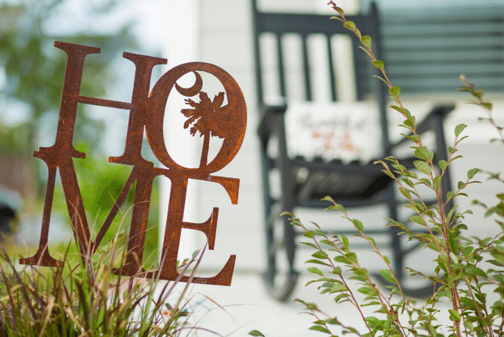 Rusted metal sign that says Home in front of a rocking chair on a porch