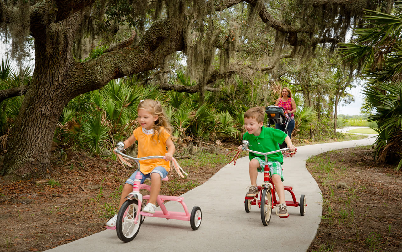 Two kids riding tricycles on a paved path in Waterset